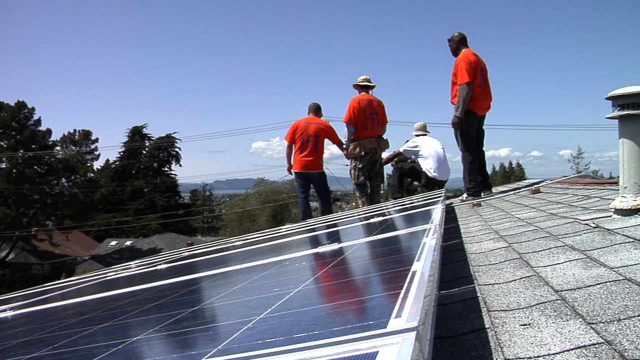 An image from the film Catching the Sun of workers in jeans and red t-shirts installing solar panels on a building's roof.